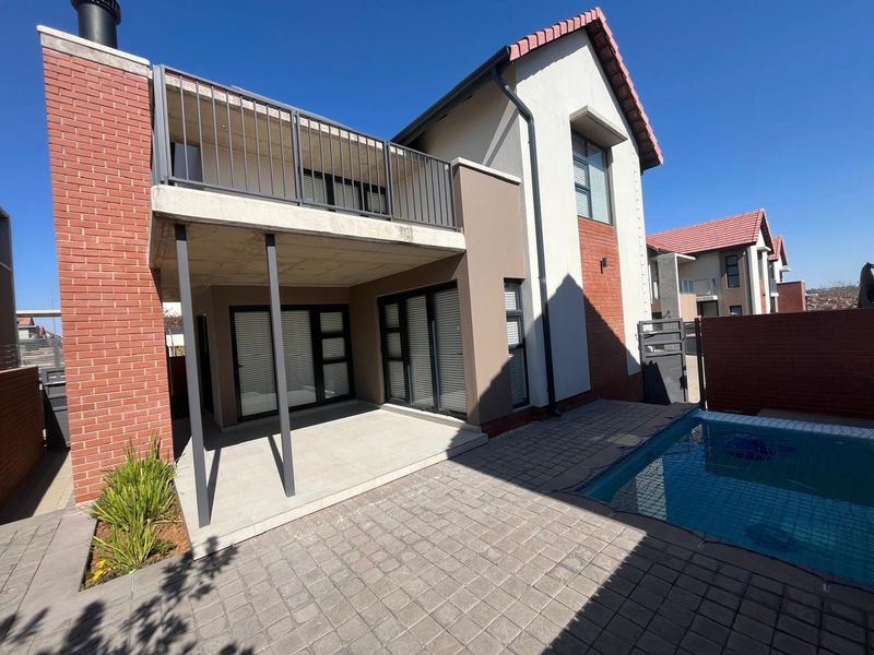 Rear view of the townhouse featuring a covered patio, an upper-level balcony with metal railings, and a private swimming pool set in a paved courtyard.