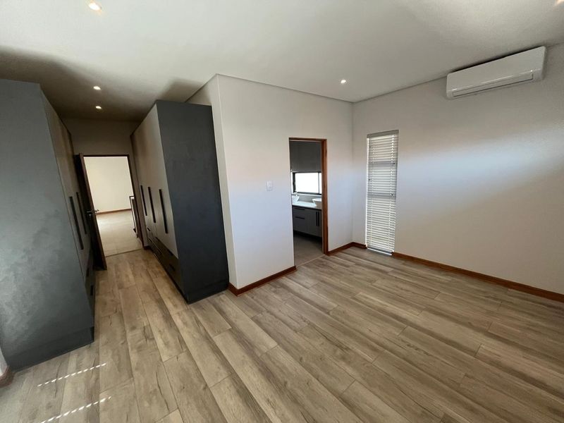 Spacious bedroom featuring modern laminate flooring, extensive built-in cabinetry, an integrated air conditioning unit, and direct access to an en-suite bathroom.