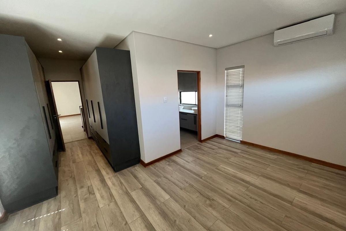 Spacious bedroom featuring modern laminate flooring, extensive built-in cabinetry, an integrated air conditioning unit, and direct access to an en-suite bathroom.