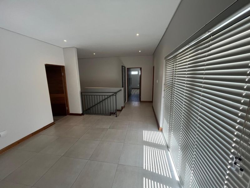 A spacious, empty upper-level landing area featuring neutral tiled flooring, recessed lighting, and a metal staircase railing with access to adjacent rooms.