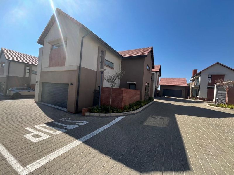 Front exterior view of a modern townhouse complex featuring paved driveways, tiled roofs, and integrated garage access.
