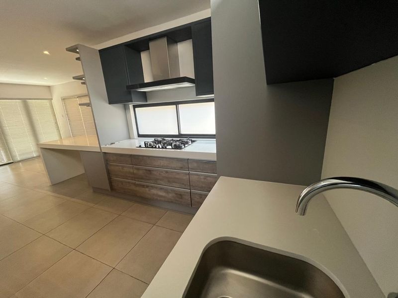Modern kitchen featuring sleek dark cabinetry, stone countertops, a gas hob with extractor fan, and tiled flooring in an open-plan layout.