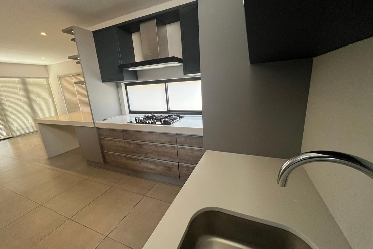 Modern kitchen featuring sleek dark cabinetry, stone countertops, a gas hob with extractor fan, and tiled flooring in an open-plan layout.