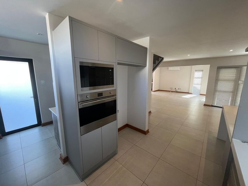 Spacious open-plan living area featuring modern built-in kitchen appliances, neutral tiled flooring, and large windows with fitted blinds.