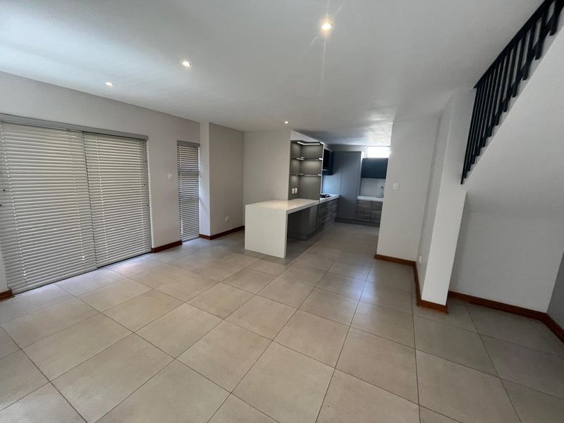 Spacious open-plan living and kitchen area featuring modern tiled flooring, recessed lighting, and a functional kitchen island with integrated cabinetry.