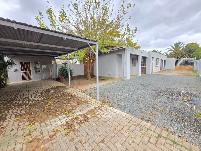 Front exterior view of the apartment featuring a covered carport, paved driveway, gravel area, and secure gated access.