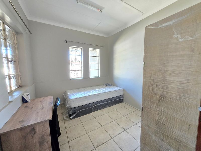 A functional bedroom featuring tiled flooring, security bars on the windows, and a built-in cupboard.