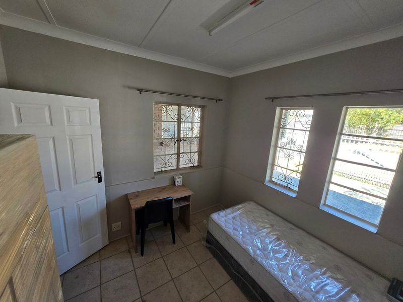 A functional bedroom featuring tiled flooring, security bars on the windows, and neutral wall tones, providing a simple and practical living space.