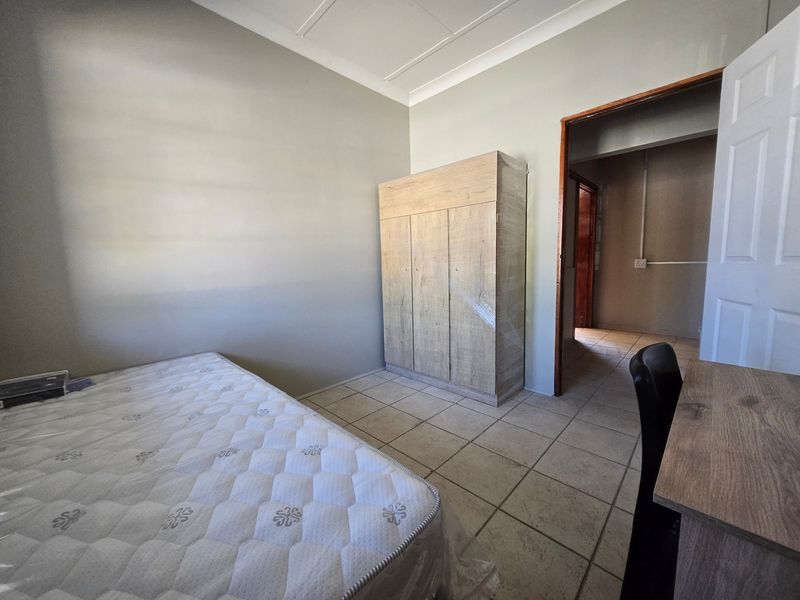 A bedroom featuring tiled flooring, a built-in wardrobe, and neutral wall finishes, providing a functional space with direct access to an adjoining hallway.