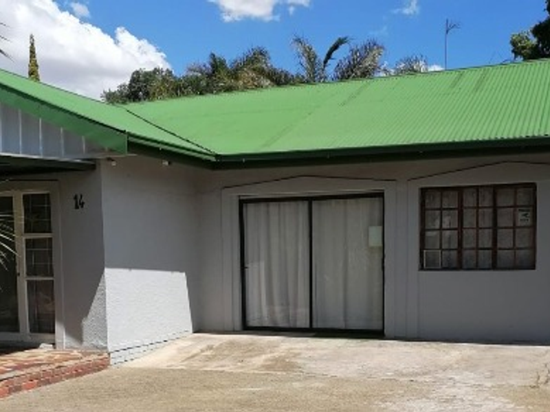 Front elevation of a single-story house featuring a green corrugated metal roof, sliding glass doors, and a concrete driveway.
