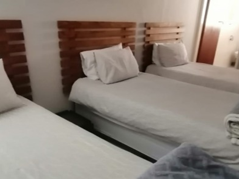 A bedroom featuring three single beds arranged in a row, with a glimpse of an adjoining bathroom area.