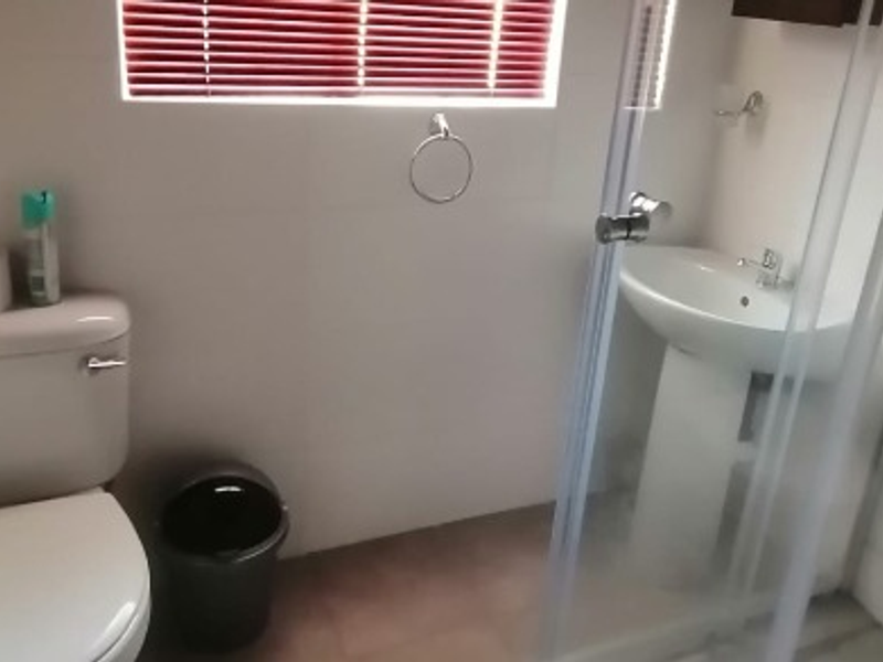 A functional bathroom featuring a pedestal basin, a shower enclosure with glass door, and a standard toilet, finished with tiled walls and flooring.