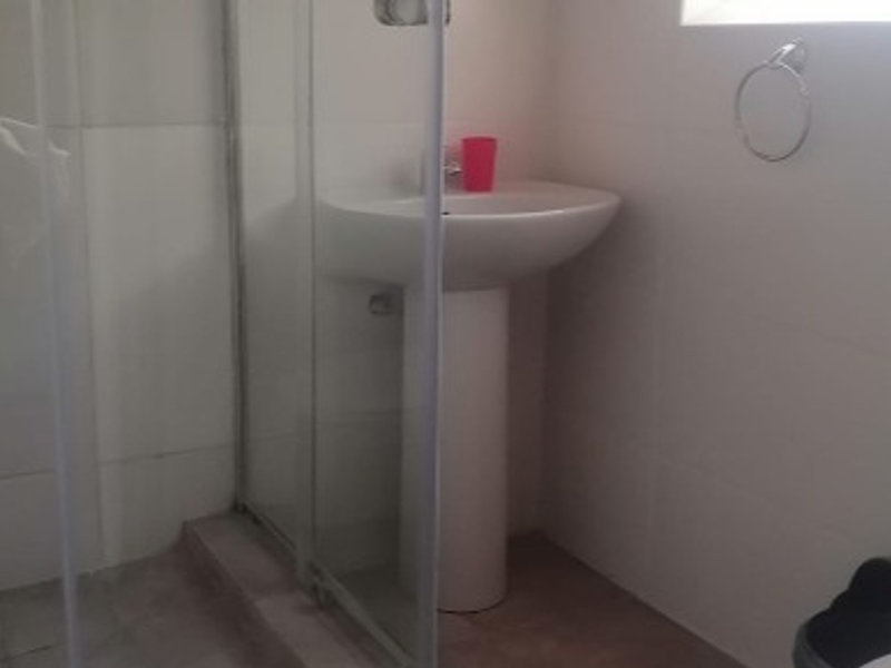 A functional bathroom featuring a pedestal sink, tiled walls, and a glass-enclosed shower area.