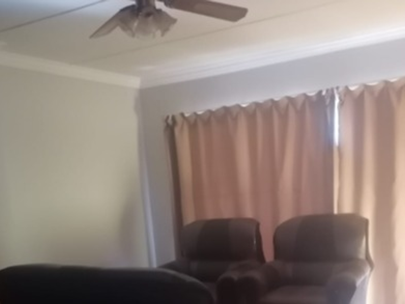A living room featuring crown molding and a ceiling fan, with natural light filtering through window curtains.