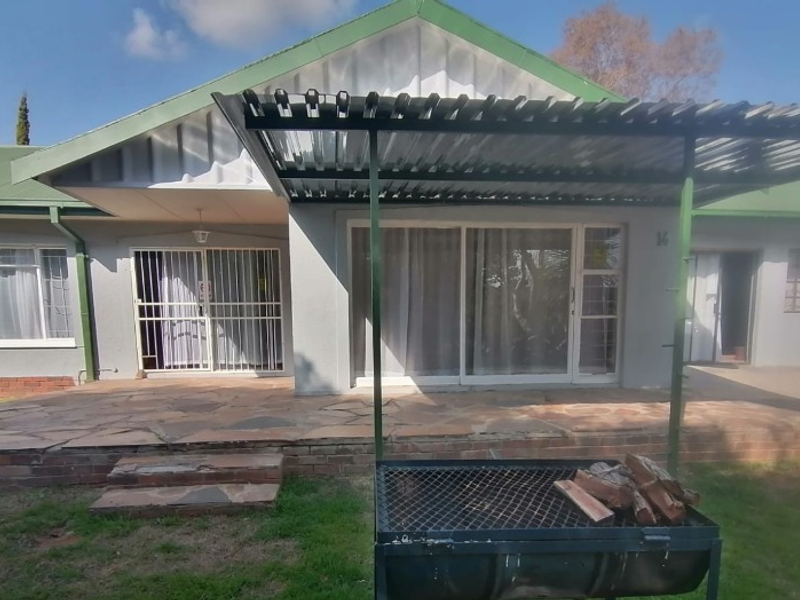 Rear exterior view of the house featuring a stone paved patio, metal pergola, and sliding glass door access.