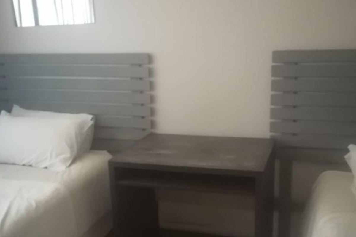 A bedroom featuring two beds with grey headboards and a central bedside table.