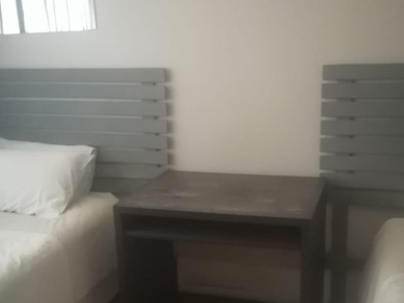 A bedroom featuring two beds with grey headboards and a central bedside table.