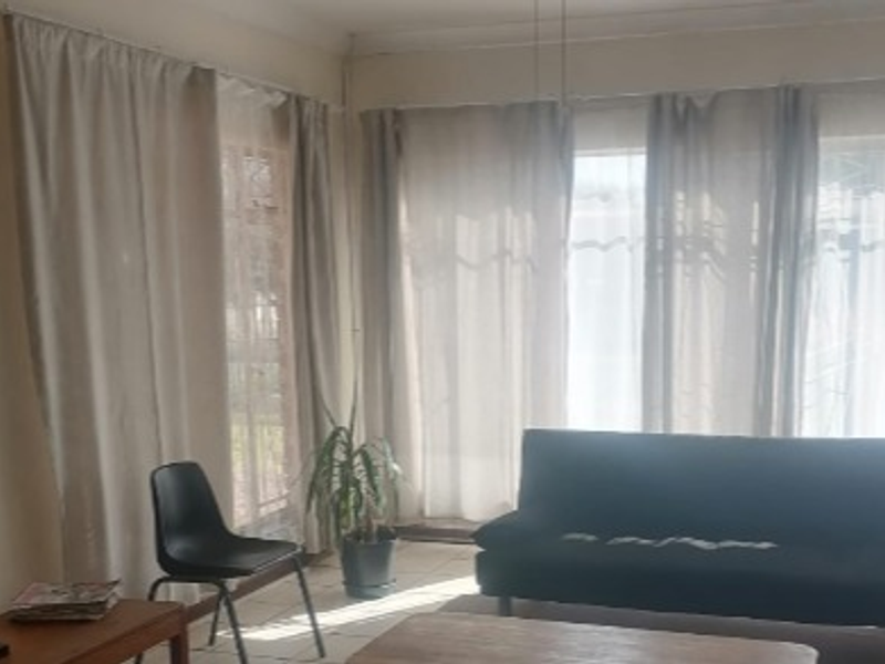 A living room area featuring tiled flooring and large windows that allow for natural light.