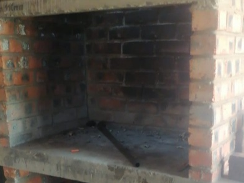 A rustic, unfinished built-in brick braai area located on a patio, featuring a concrete countertop and showing signs of heavy use.