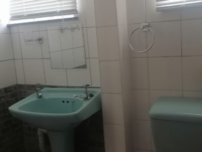 A compact bathroom featuring dated pastel-colored sanitaryware, including a pedestal basin and toilet, complemented by tiled wall finishes and window blinds.