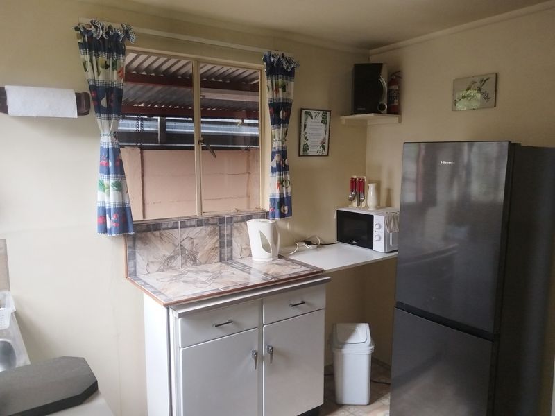A compact kitchen area featuring basic built-in cabinetry, a tiled splashback, and a window, providing a functional space for food preparation.