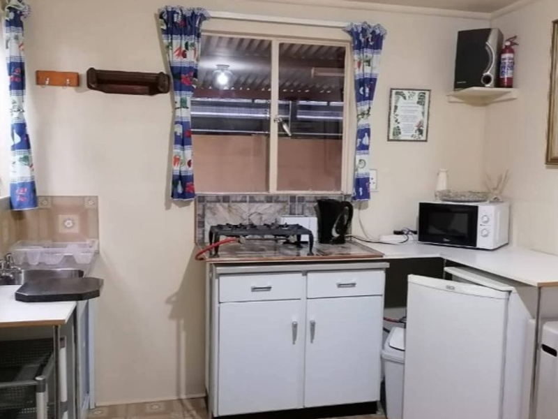 A compact, functional kitchen featuring basic cabinetry, a stainless steel sink, tiled backsplash, and a gas hob, requiring modernization to improve aesthetic appeal.