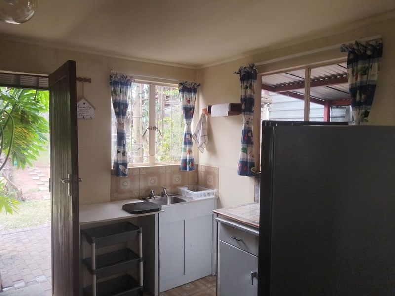 A compact kitchen area featuring a stainless steel sink, tiled backsplash, and built-in cabinetry with direct access to an outdoor patio area.