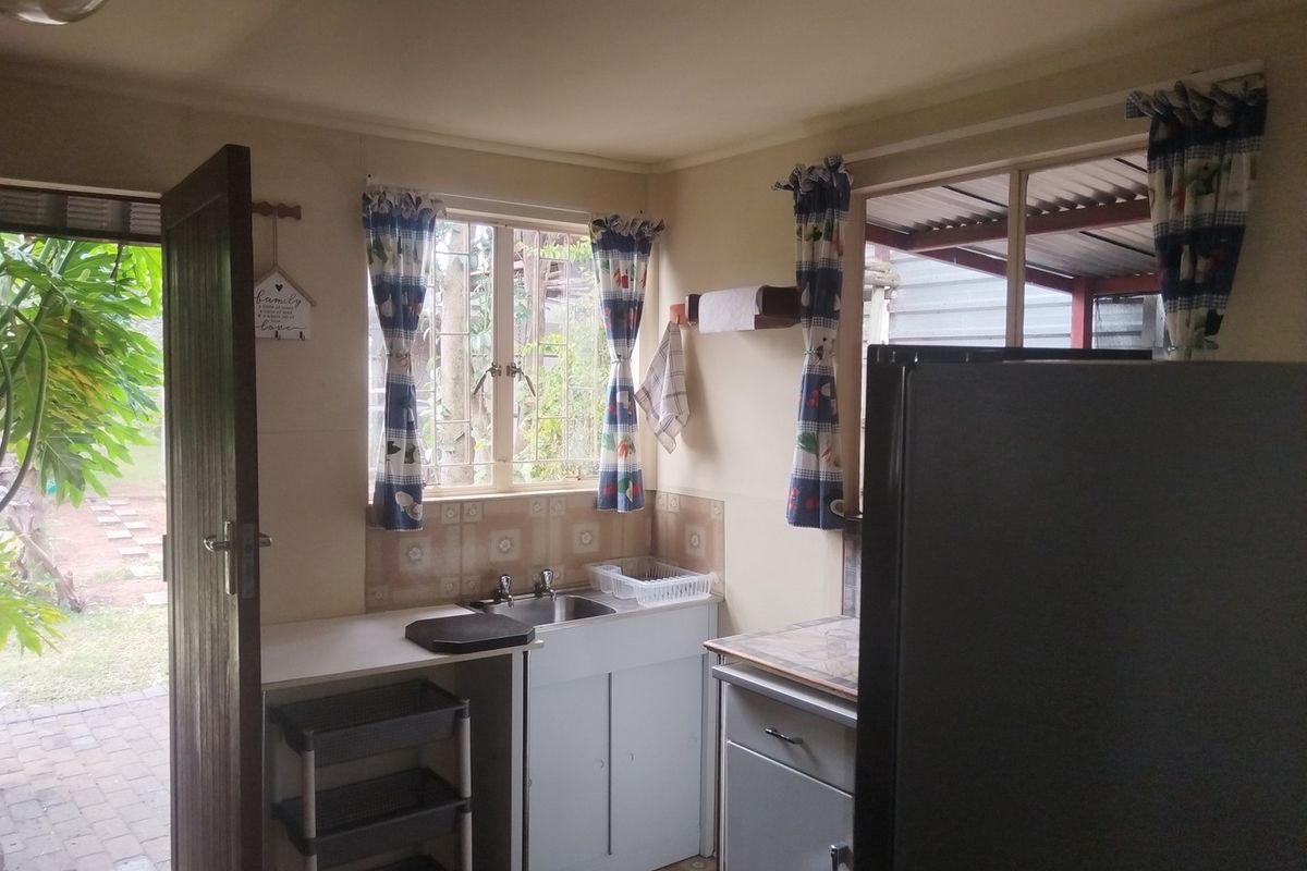 A compact kitchen area featuring a stainless steel sink, tiled backsplash, and built-in cabinetry with direct access to an outdoor patio area.