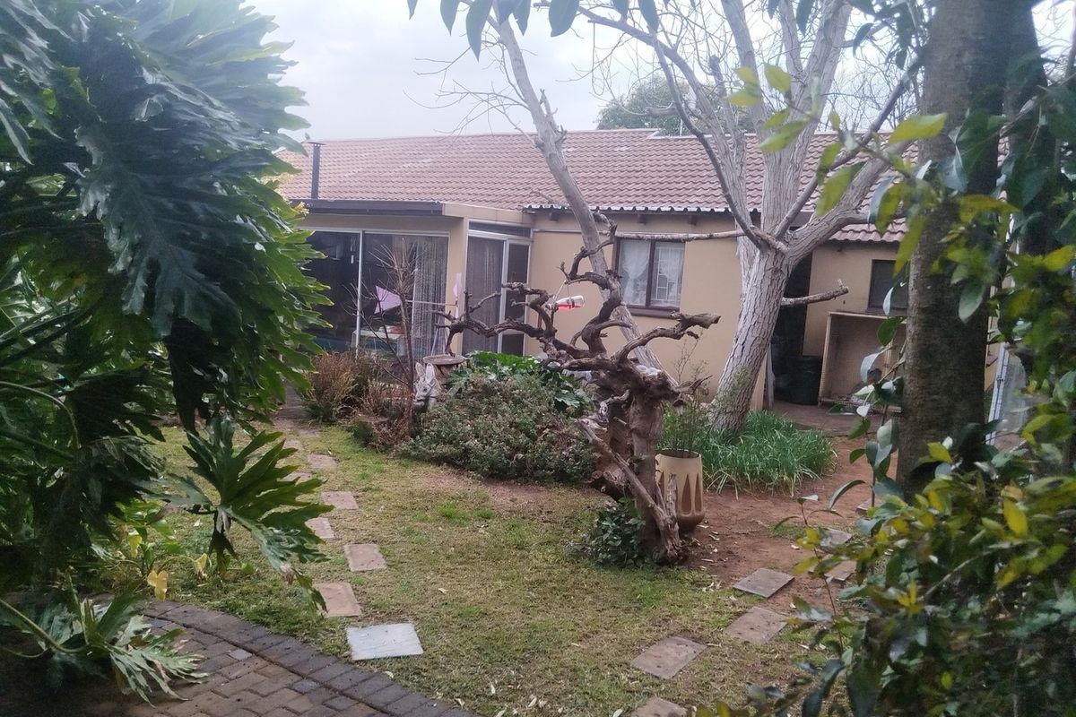 Rear view of the property featuring a tiled roof, sliding glass doors, and a garden area with a paved walkway.