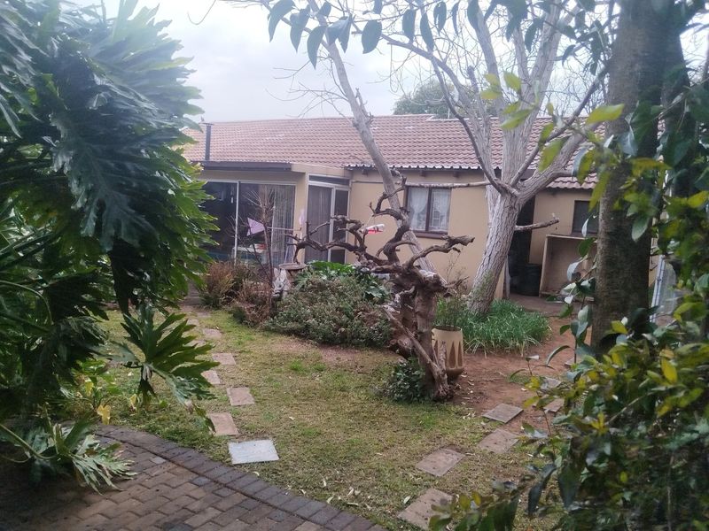 Rear view of the property featuring a tiled roof, sliding glass doors, and a garden area with a paved walkway.