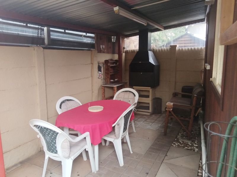Covered outdoor patio area featuring a built-in braai, paved flooring, and enclosed by precast concrete walls, providing a functional space for outdoor dining.