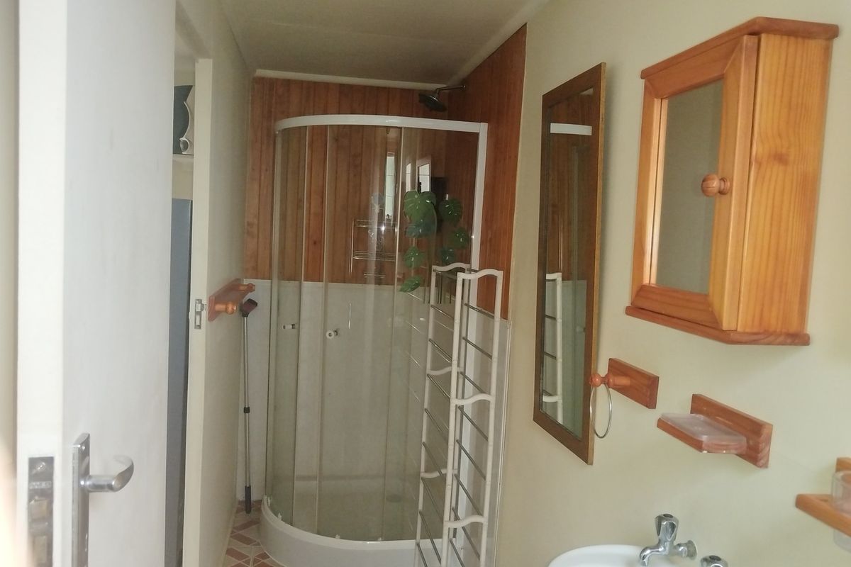 A compact bathroom featuring a corner shower enclosure, pedestal sink, timber wall paneling, and built-in wooden cabinetry.