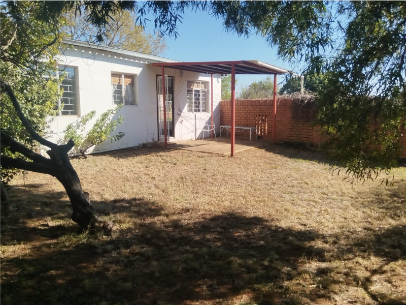 Rear exterior view of the house featuring a covered patio area, brick boundary wall, and established garden space.