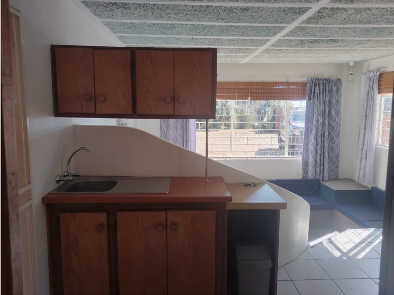 A compact kitchen area featuring dated wooden cabinetry, laminate countertops, and a stainless steel sink, with tiled flooring and a textured ceiling.