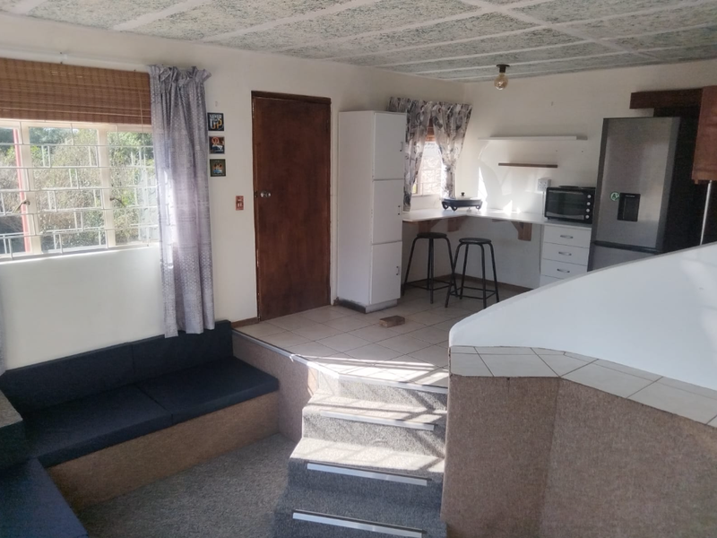 Open plan living and kitchen area featuring a raised platform, built-in seating, tiled kitchen workspace, and security bars on the windows.