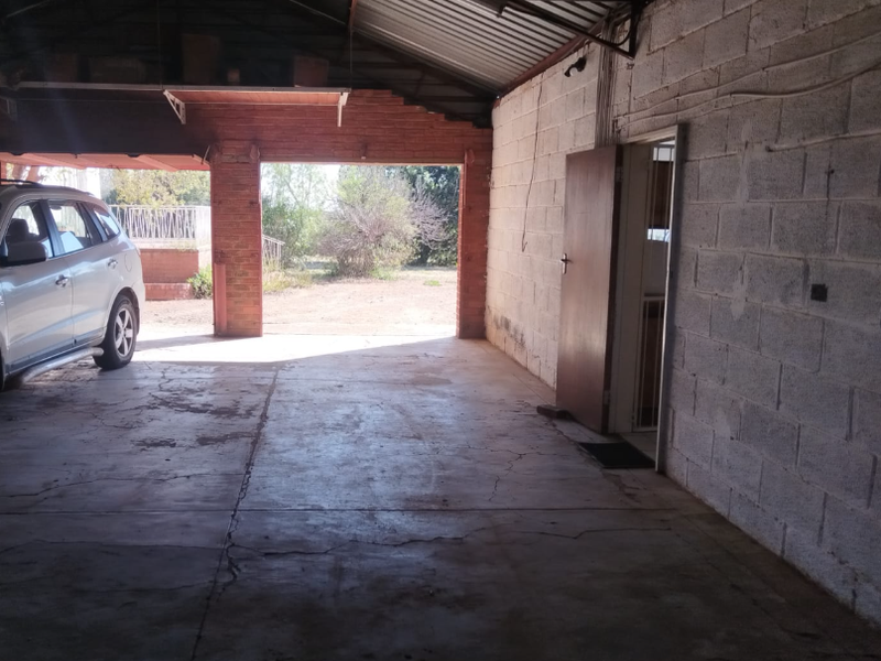 A spacious, open-plan garage featuring exposed brick and blockwork walls, concrete flooring, and a high corrugated metal roof structure.