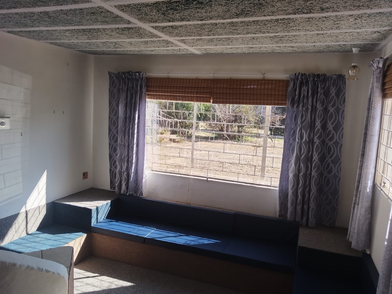 A living area featuring built-in seating, security bars on windows, and a textured ceiling finish, offering a functional space with potential for modernization.