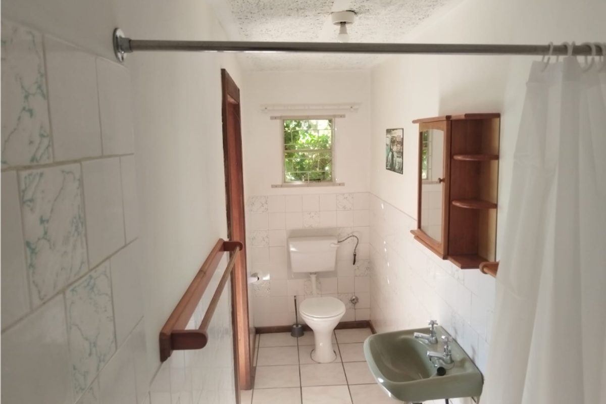 A functional bathroom featuring a pedestal basin, toilet, and tiled finishes. The space is dated and would benefit from modern updates.