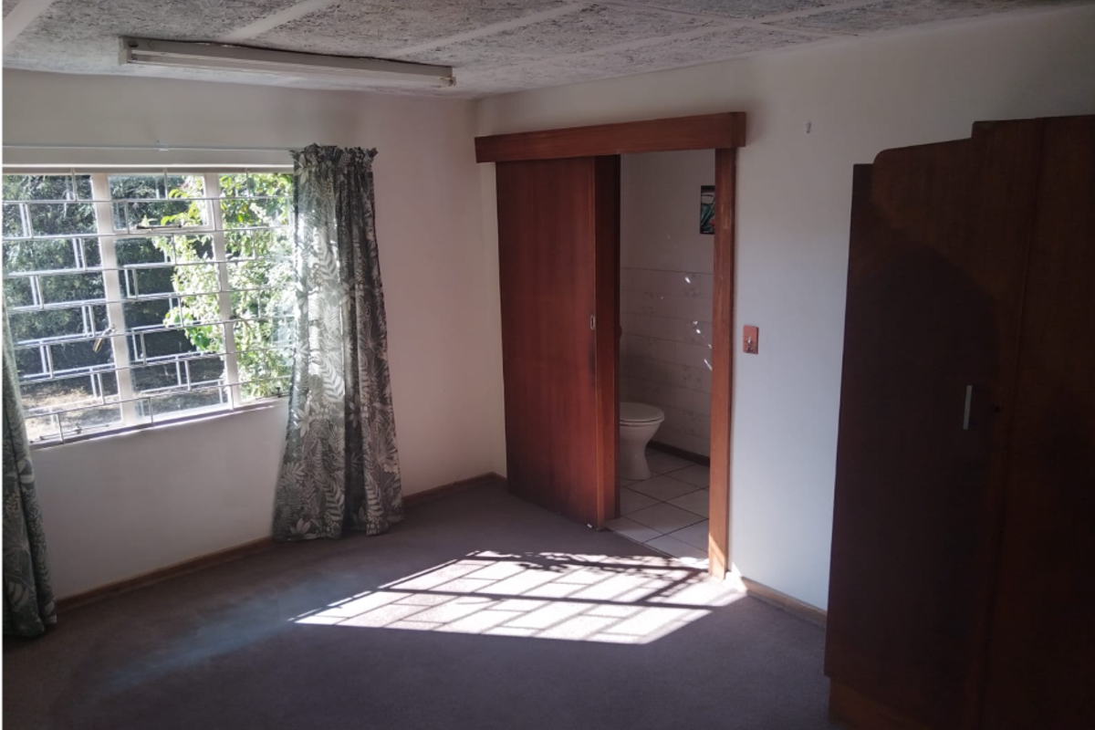 A bedroom featuring a sliding door leading to an ensuite bathroom, carpeted flooring, and a window with security bars.