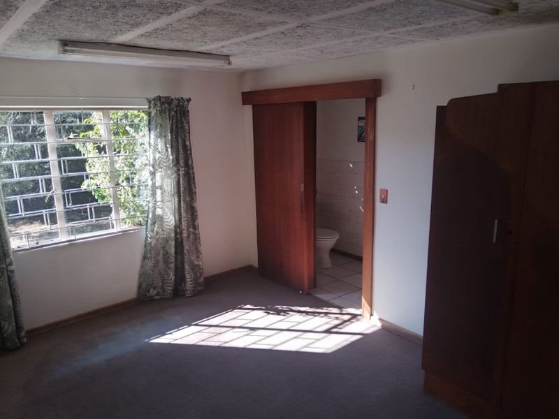 A bedroom featuring a sliding door leading to an ensuite bathroom, carpeted flooring, and a window with security bars.