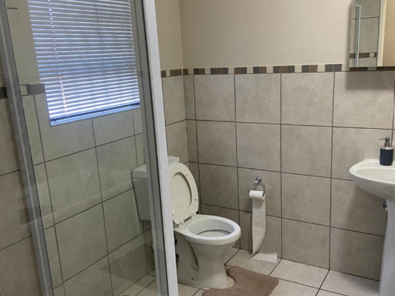 A functional bathroom featuring a glass shower enclosure, pedestal sink, toilet, and neutral ceramic tiling throughout.