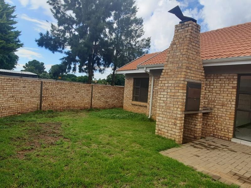 Rear garden area featuring a paved patio, built-in brick braai, and perimeter brick walling, accessible via sliding glass doors.