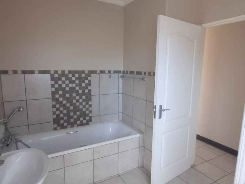 A functional bathroom featuring a bathtub, separate shower enclosure, and pedestal basin with neutral wall tiling and a decorative mosaic accent border.