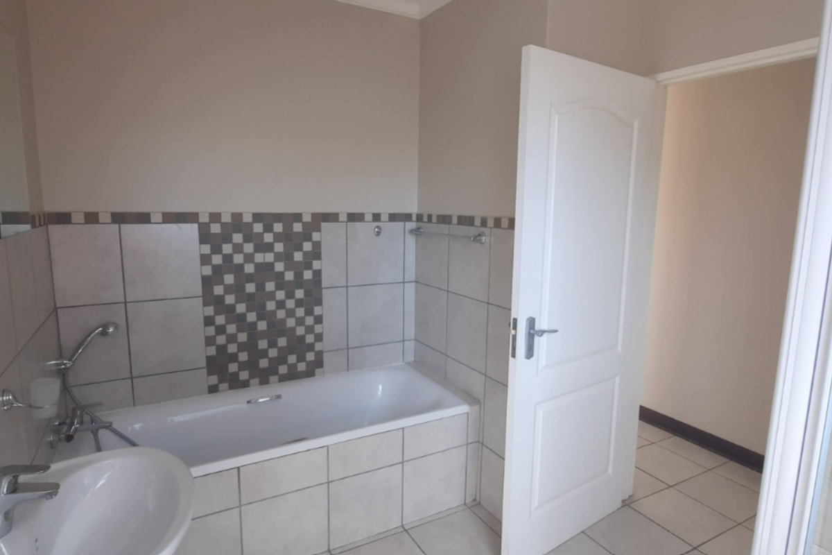 A functional bathroom featuring a bathtub, separate shower enclosure, and pedestal basin with neutral wall tiling and a decorative mosaic accent border.