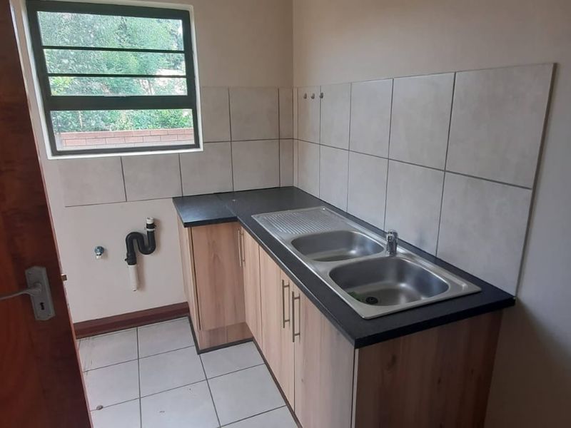 A functional laundry room featuring a double stainless steel sink, laminate cabinetry, tiled splashback, and dedicated plumbing connections for appliances.
