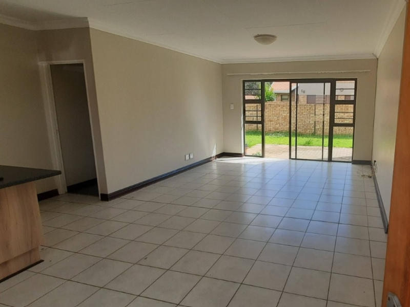 Spacious open-plan living area featuring neutral walls, tiled flooring, and a sliding glass door providing direct access to the rear garden.