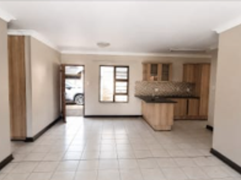 An open-plan living and kitchen area featuring tiled flooring, neutral walls, and built-in wooden cabinetry with a functional peninsula layout.