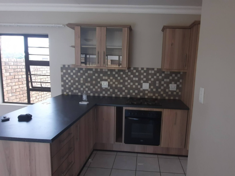 A functional kitchen featuring wood-finish cabinetry, dark laminate countertops, a built-in oven and hob, and a tiled backsplash with neutral floor tiles.