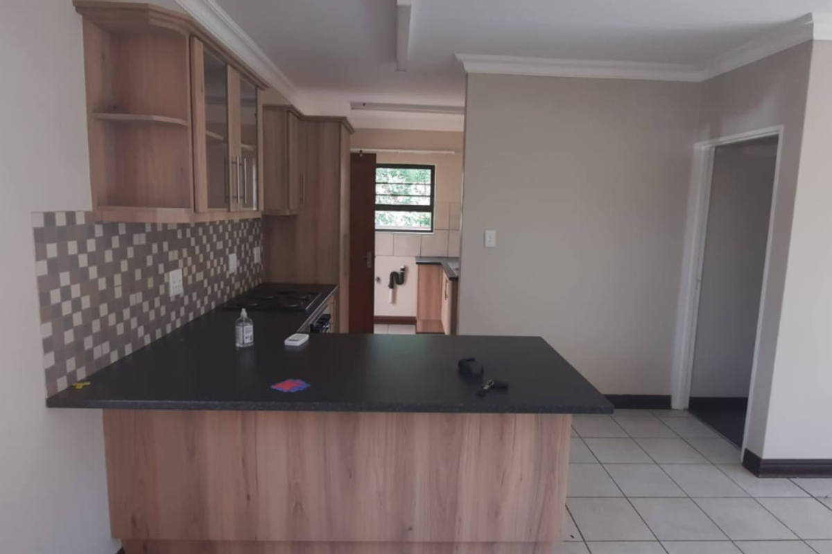 A functional kitchen featuring wood-look cabinetry, dark laminate countertops, a breakfast bar, and tiled flooring, offering a clean and practical layout.