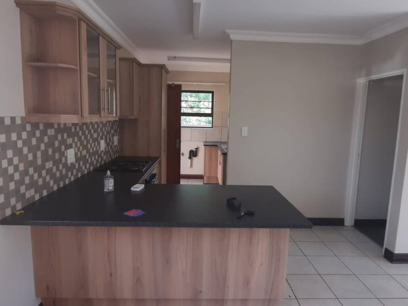 A functional kitchen featuring wood-look cabinetry, dark laminate countertops, a breakfast bar, and tiled flooring, offering a clean and practical layout.